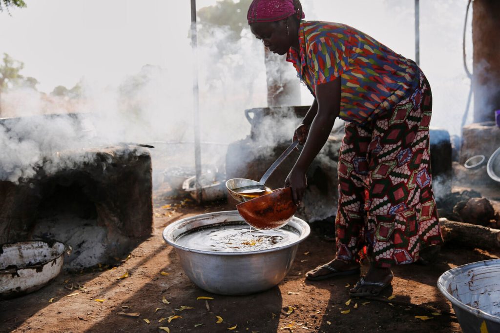 A Ghanaian woman scoops shea oil into a copper bowl using a ladle.