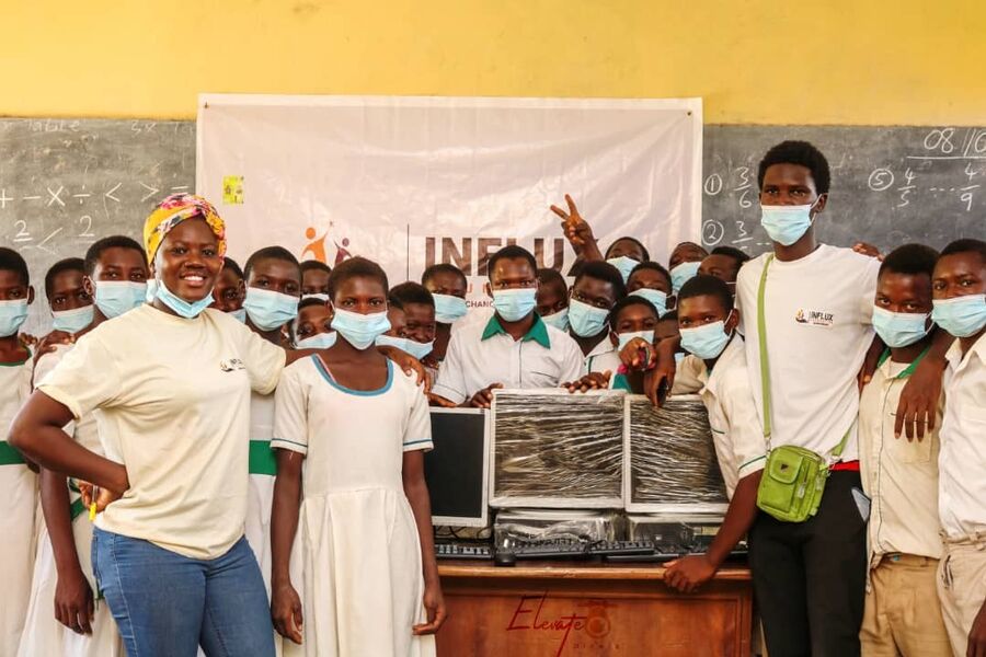 A group of Ghanaian students gather around new desktop computers inside a school classroom.