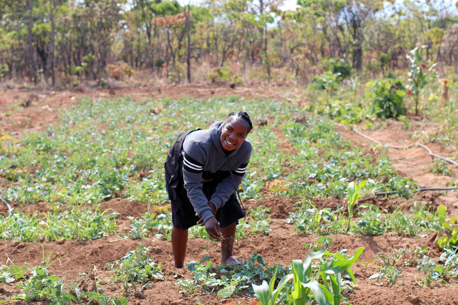 A young Zambian woman stands outside on her farm.