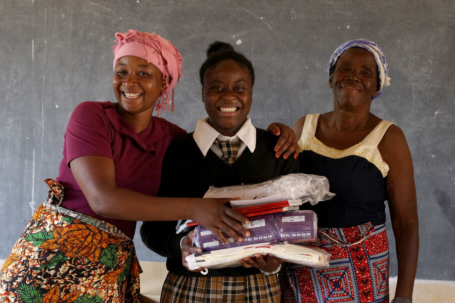 Sara (left) and Christine (right) hand essential school supplies to CAMFED supported student, Mapalo.