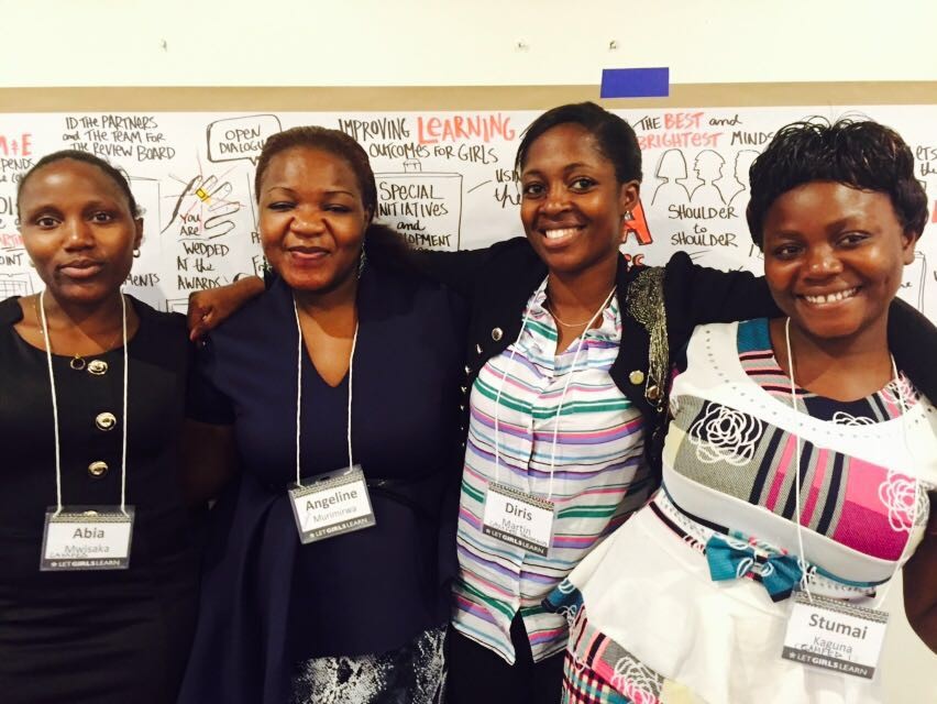Four women from CAMFED's movement smile in front of a poster.