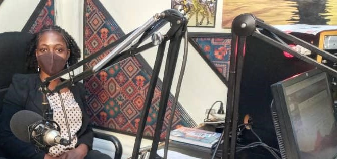 Diris, a Tanzanian woman sits in an audio recording both with a microphone and audio equipment.