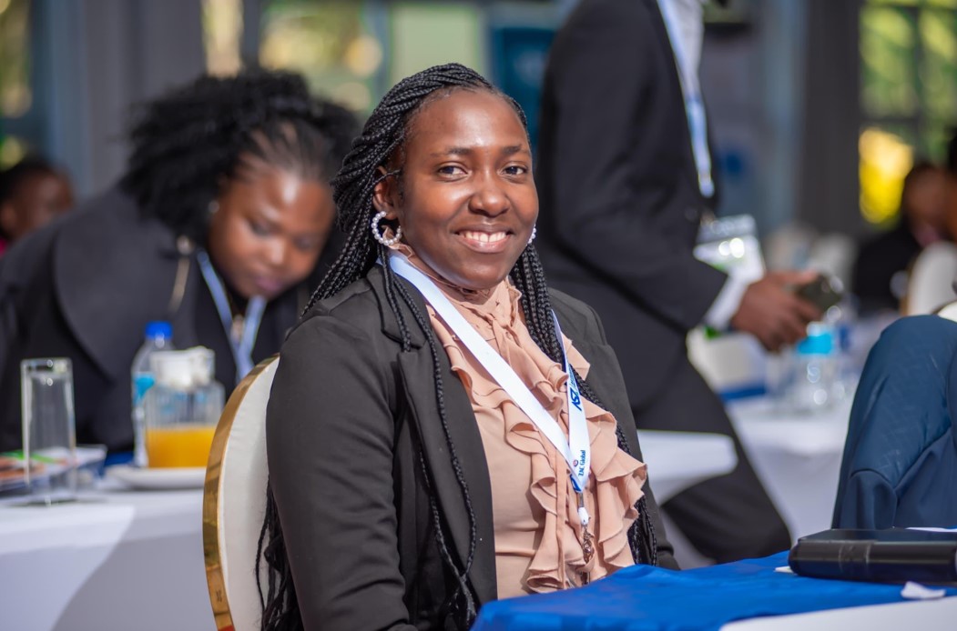 A Zimbabwean woman wearing a suit, sits and smiles at the camera.