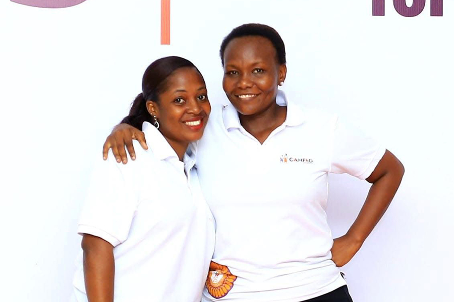 Diris and Anna, CAMFED employees in Tanzania wearing white t-shirts, smile.